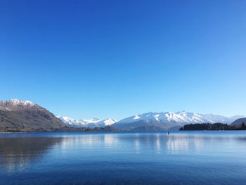 Scenic view of lake and snowcapped mountains against clear blue sky