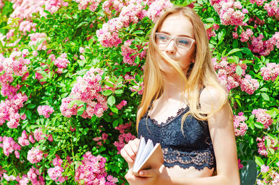 Teenage girl holding book while standing by flowering plants