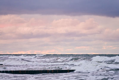Scenic view of purple cloudy sky and sea with foaming waves. vintage long wooden breakwaters