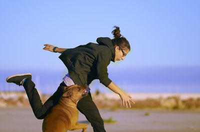 Woman playing with dog at beach against blue sky