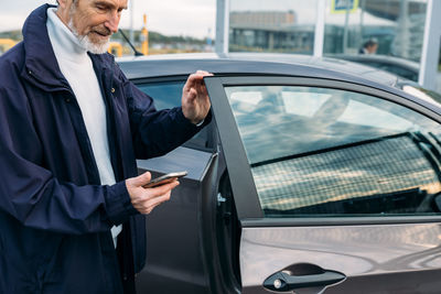 Midsection of senior man using smart phone standing by car