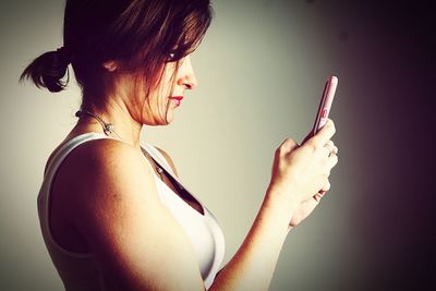Profile view of beautiful woman using phone against gray background