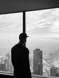 Rear view of man looking through glass window