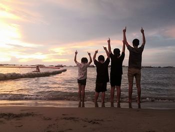 Rear view of people standing at beach during sunset