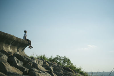 Man sitting on retaining wall by sea against sky