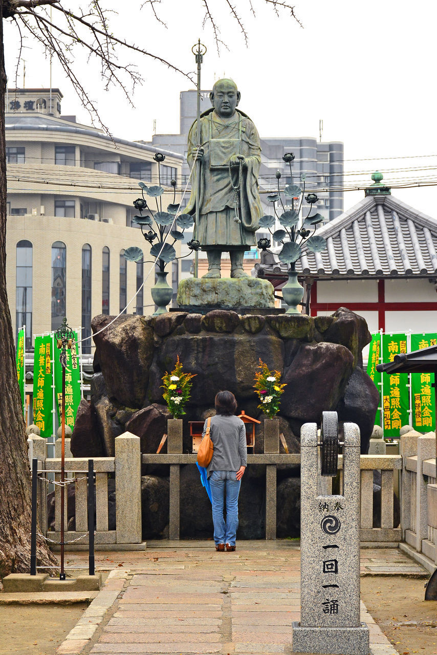 REAR VIEW OF MAN STANDING AT STATUE