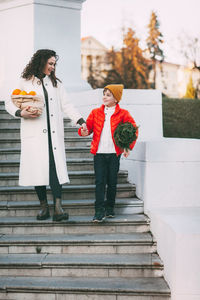 A beautiful mother with her son in a bright orange jacket and a fashionable yellow hat are walking 