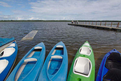 Boats moored on pier by river against sky