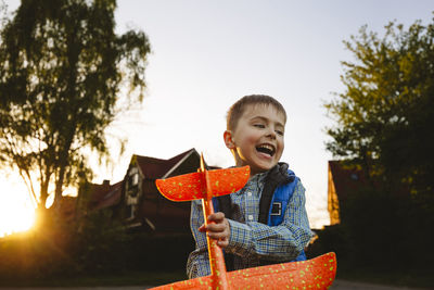 Smiling boy holding toy airplane at sunset