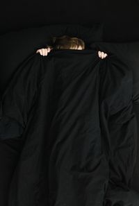 High angle view of boy with black blanket lying on bed