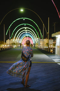 Rear view of woman standing on illuminated bridge