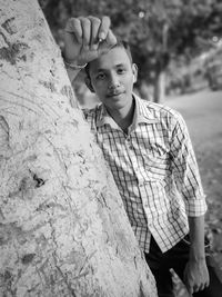 Portrait of young man standing by tree trunk