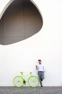 Young bearded man leaning against a white wall using the mobile phone