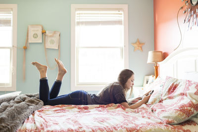 Woman using mobile phone while lying on bed at home