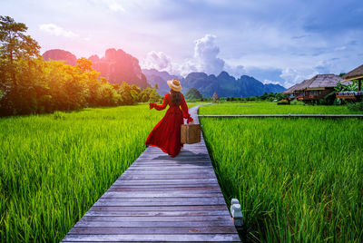 Rear view of woman walking on field against sky