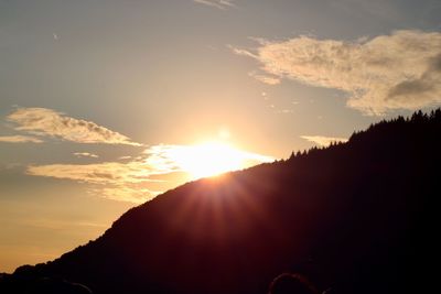 Sunlight streaming through silhouette mountain against sky during sunset