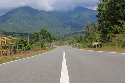 Road amidst trees and mountains against sky