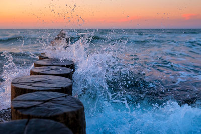 Water splashing in sea against sky during sunset