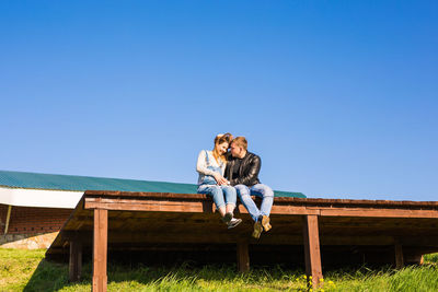 Rear view of couple sitting against blue sky