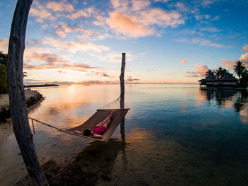 High angle view of woman relaxing on hammock in sea at sunset