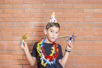 Portrait of boy wearing party equipment against brick wall