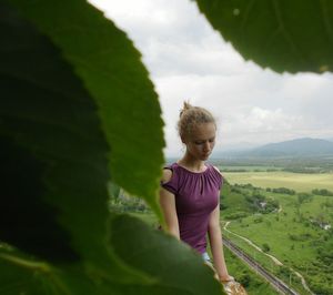 Close-up of thoughtful young woman on mountain against cloudy sky