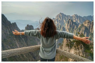 Rear view of woman with arms outstretched at observation point against mountains