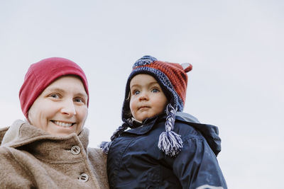 Portrait of cheerful mother with toddler daughter against clear sky during winter