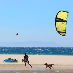 Man flying kite at beach against clear blue sky