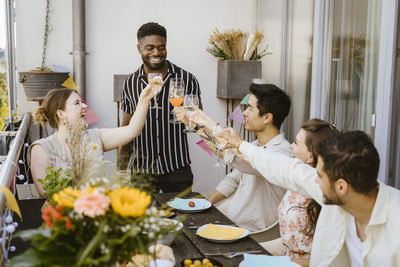 Smiling young man toasting drinks with group of male and female friends during dinner party in balcony