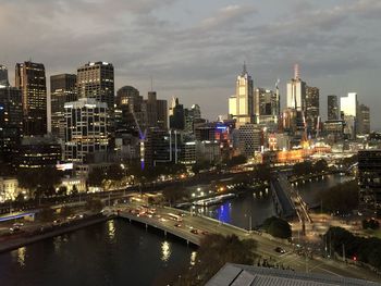 Illuminated bridge over river by buildings against sky at night