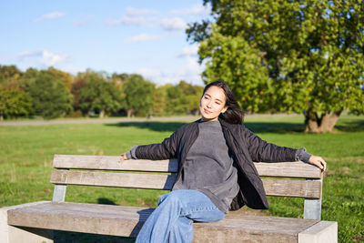 Portrait of young woman sitting on bench against lake