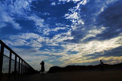 Silhouette man standing by railing against sky during sunset