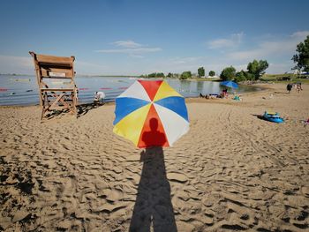 Shadow of person standing in front of umbrella at beach against sky