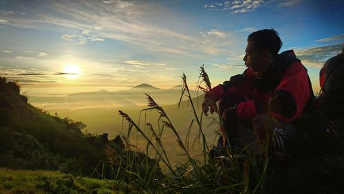 Male hiker sitting on mountain against sky during sunset
