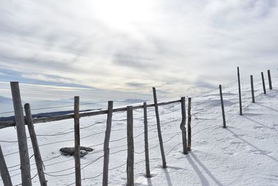 Wooden fence on snow covered land against sky