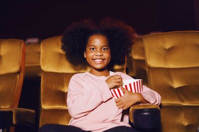 Girl holding food while sitting on chair in movie theater