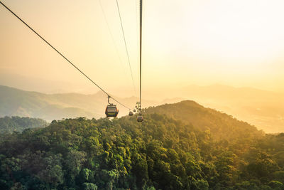 Overhead cable car over mountains against sky during sunset