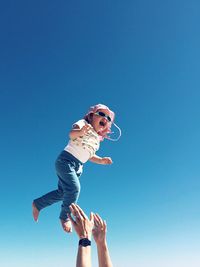 Low angle view of father catching daughter against blue sky