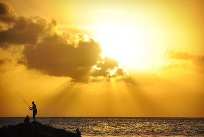 Silhouette person standing by sea against sky during sunset