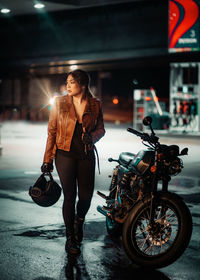 Full length of woman carrying helmet by motorcycle