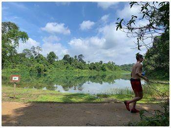 Side view of shirtless man against lake against sky