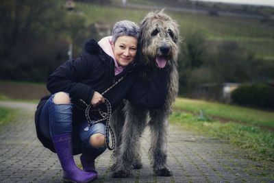 Portrait of smiling woman with dog crouching on footpath