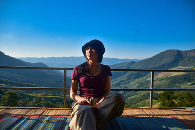 Young woman sitting on observation point against clear blue sky