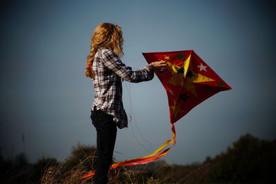 Woman holding kite while standing on field