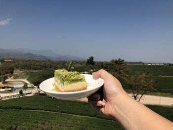 Midsection of person holding food on landscape against sky