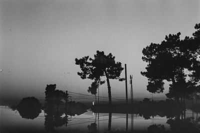 Silhouette trees by lake against sky