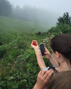 Cropped image of person with camera by woman photographing berries through mobile phone