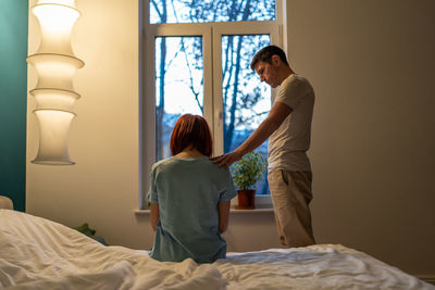 Side view of woman sitting on bed at home