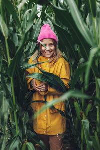 Funny little girl dressed in a yellow raincoat and a hot pink cap spoils and bites corn 